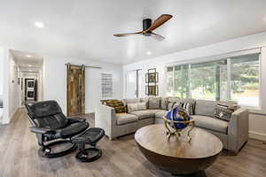 Living area with a barn door, ceiling fan, light wood-style flooring, baseboards, and recessed lighting