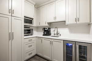 Kitchen featuring beverage cooler, a sink, light countertops, and stainless steel microwave
