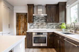 Kitchen with appliances with stainless steel finishes, wall chimney range hood, a sink, dark brown cabinets, and light countertops