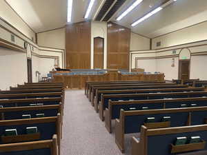 Chapel with carpet flooring, upholstered benches, and high, vaulted ceiling.