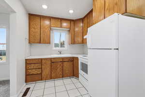 Kitchen featuring white appliances, brown cabinets, light countertops, light tile patterned floors, and recessed lighting