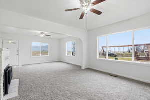 Unfurnished living room featuring a fireplace, carpet floors, arched walkways, and a ceiling fan