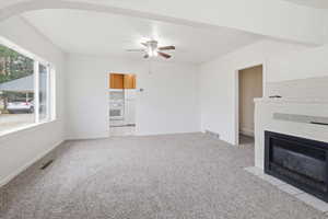 Unfurnished living room featuring light colored carpet, a ceiling fan, and a fireplace with flush hearth