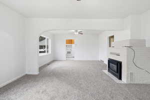 Unfurnished living room with a ceiling fan, light colored carpet, a brick fireplace, and arched walkways