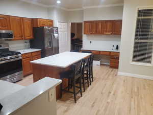 Kitchen with stainless steel appliances, crown molding, light countertops, brown cabinets, and a kitchen bar