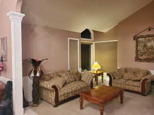 Carpeted living room with ornate columns and lofted ceiling