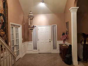 Entrance foyer featuring a decorative wall, a wainscoted wall, vaulted ceiling, and ornate columns