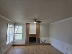 Unfurnished living room featuring wood finished floors, a textured ceiling, ceiling fan, a fireplace, and a decorative wall