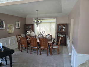 Dining area featuring a textured ceiling, a chandelier, light carpet, and a wainscoted wall