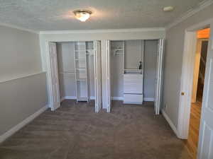 Unfurnished bedroom with two closets, a textured ceiling, carpet flooring, ornamental molding, and baseboards
