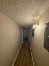 Hallway featuring dark wood-type flooring, electric panel, baseboards, and a textured ceiling