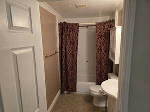 Bathroom featuring a textured ceiling, toilet, vanity, shower / bath combo with shower curtain, and baseboards