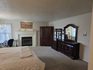 Carpeted bedroom with a textured ceiling, a fireplace with flush hearth, and baseboards