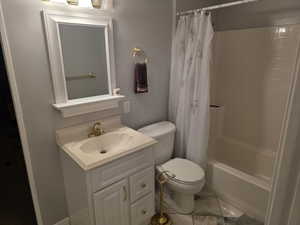 Full bath featuring toilet, vanity, shower / bathtub combination with curtain, and marble look tiles