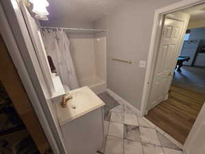 Bathroom with a textured ceiling, vanity, marble look tiles, shower / bath combo with shower curtain, and baseboards