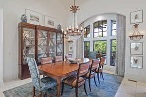 Tiled dining space featuring a chandelier, arched walkways, baseboards, and a high ceiling