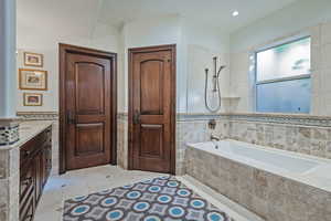 Full bath with tile walls, wainscoting, tile patterned flooring, tiled shower / bath combo, and vanity