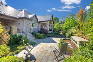 Rear view of house featuring stone siding, a patio, and a high end roof