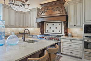 Kitchen with stainless steel appliances, a sink, custom exhaust hood, cream cabinetry, and light stone countertops