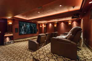 Carpeted home theater room featuring a raised ceiling, baseboards, ornamental molding, and recessed lighting