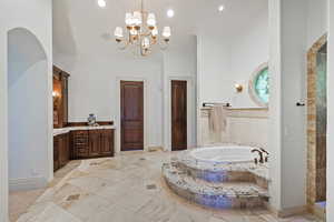 Full bathroom featuring a bath, a towering ceiling, vanity, a chandelier, and baseboards