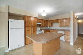 Kitchen with white appliances, baseboards, under cabinet range hood, a kitchen island, and light tile patterned floors