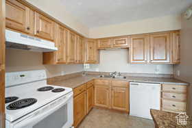 Kitchen featuring white appliances, under cabinet range hood, a sink, light brown cabinets, and light tile patterned floors