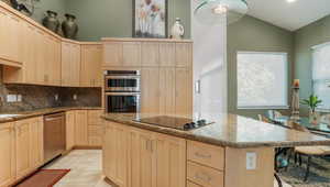 Kitchen featuring light brown cabinets, appliances with stainless steel finishes, backsplash, a center island, and light stone counters