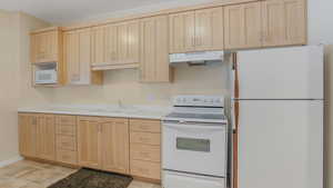 Kitchen with white appliances, light brown cabinets, under cabinet range hood, a sink, and light countertops