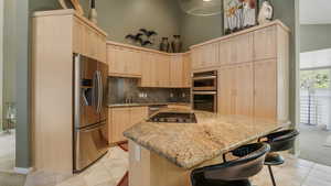 Kitchen featuring stainless steel appliances, light brown cabinets, a kitchen island, light tile patterned flooring, and a high ceiling