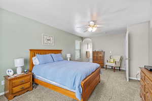 Bedroom featuring baseboards, arched walkways, light colored carpet, a ceiling fan, and a textured ceiling