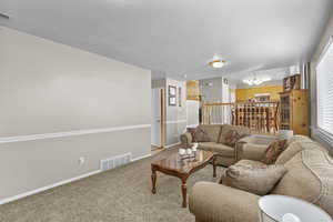 Living room featuring a chandelier, light carpet, baseboards, a textured ceiling, and healthy amount of natural light