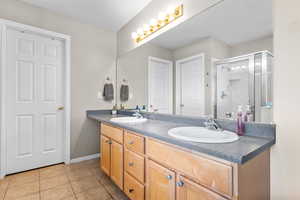 Bathroom featuring tile patterned floors, a shower stall, double vanity, and baseboards