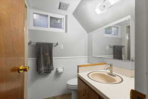 Bathroom featuring toilet, vaulted ceiling, vanity, wainscoting, and tile patterned floors
