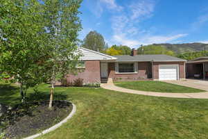 Ranch-style house featuring an attached garage, driveway, a front lawn, a chimney, and brick siding