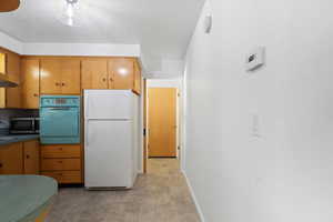 Kitchen with freestanding refrigerator, wall oven, stainless steel microwave, light colored carpet, and baseboards