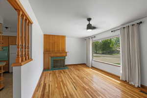 Unfurnished living room with ceiling fan, a tile fireplace, wood finished floors, and baseboards