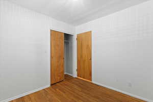 Unfurnished bedroom with wood finished floors, baseboards, and a closet