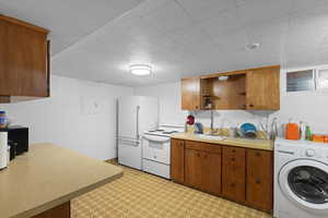 Kitchen featuring washer / dryer, white appliances, brown cabinetry, and light countertops