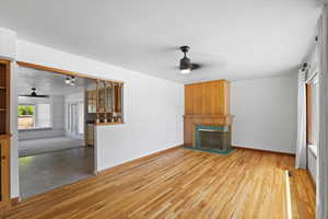 Unfurnished living room featuring a ceiling fan, a fireplace with raised hearth, and wood finished floors