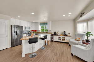 Kitchen with appliances with stainless steel finishes, a breakfast bar, light wood finished floors, white cabinetry, and recessed lighting