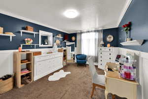 Bedroom featuring a textured ceiling, ornamental molding, carpet flooring, and a wainscoted wall