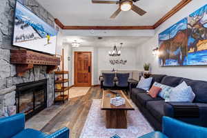 Living area with hardwood / wood-style floors, a chandelier, a fireplace, ceiling fan, and ornamental molding