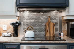 Kitchen view of backsplash, black electric cooktop, oven, and white cabinetry