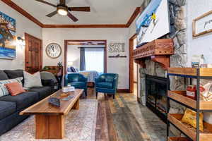 Living area with a ceiling fan, crown molding, hardwood / wood-style floors, a stone fireplace, and baseboards