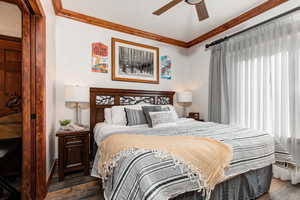 Bedroom with dark wood finished floors, ornamental molding, and a ceiling fan
