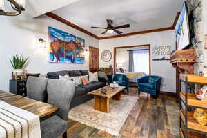 Living room with ceiling fan, ornamental molding, dark wood-style flooring, a fireplace, and baseboards