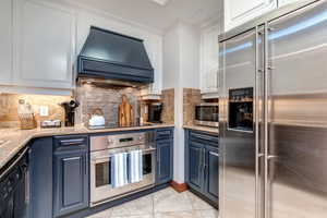 Kitchen featuring appliances with stainless steel finishes, custom range hood, blue cabinets, and white cabinets