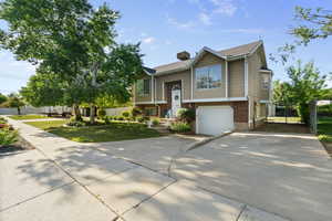 Raised ranch with concrete driveway, a garage, brick siding, and a front yard