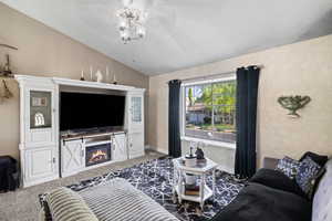 Living room featuring lofted ceiling, carpet flooring, a lit fireplace, ceiling fan, and baseboards